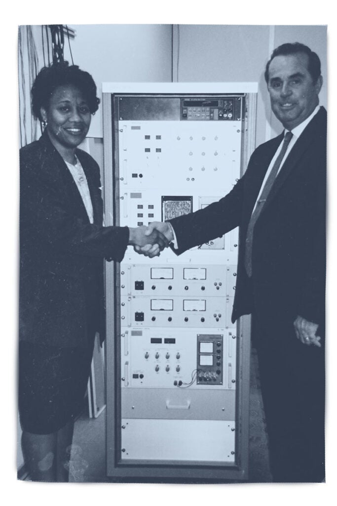 Marcie (Swilley) Washington shaking hands with a man in front a piece of technology.